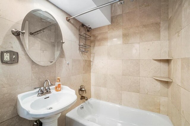 bathroom with tiled shower / bath combo, tile walls, and sink