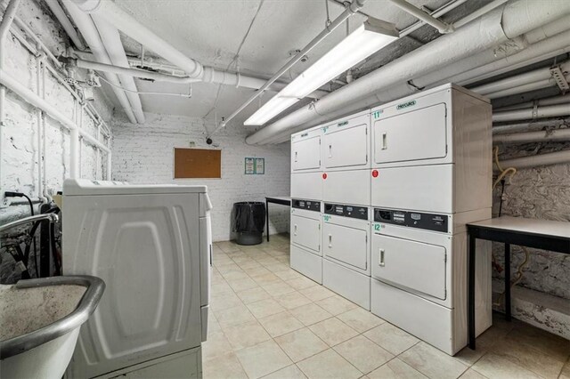 laundry area featuring sink, washer and dryer, light tile patterned floors, stacked washer / drying machine, and brick wall