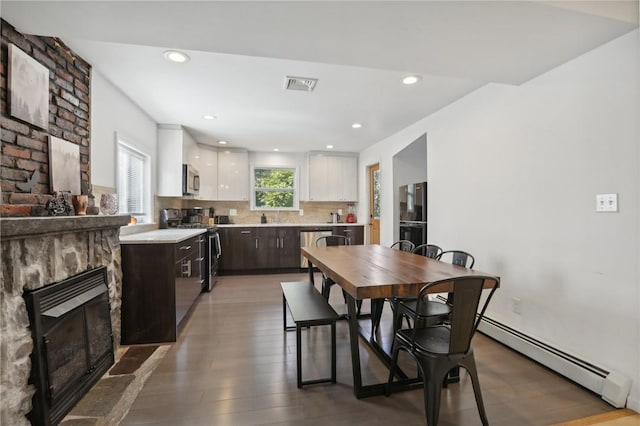 dining space featuring sink, wood-type flooring, a fireplace, and a baseboard heating unit