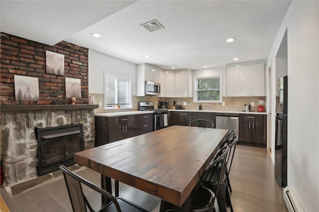 kitchen with white cabinetry, stainless steel appliances, a baseboard radiator, light hardwood / wood-style flooring, and dark brown cabinets