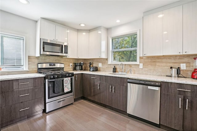 kitchen featuring dark brown cabinetry, sink, stainless steel appliances, white cabinets, and light wood-type flooring