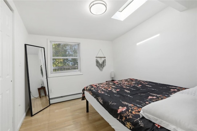 bedroom with light wood-type flooring, a skylight, and a baseboard heating unit