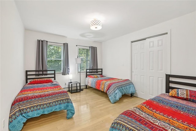 bedroom featuring hardwood / wood-style floors, baseboard heating, and a closet