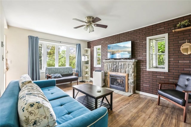 living room featuring a stone fireplace, ceiling fan, brick wall, and light hardwood / wood-style floors