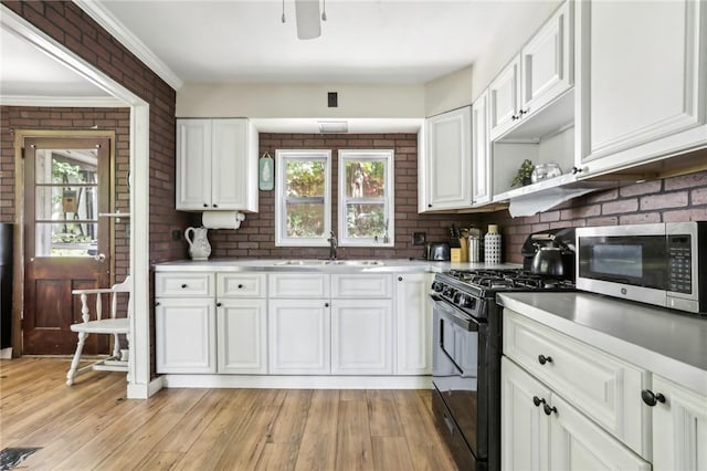 kitchen with light wood-type flooring, ornamental molding, brick wall, sink, and white cabinets