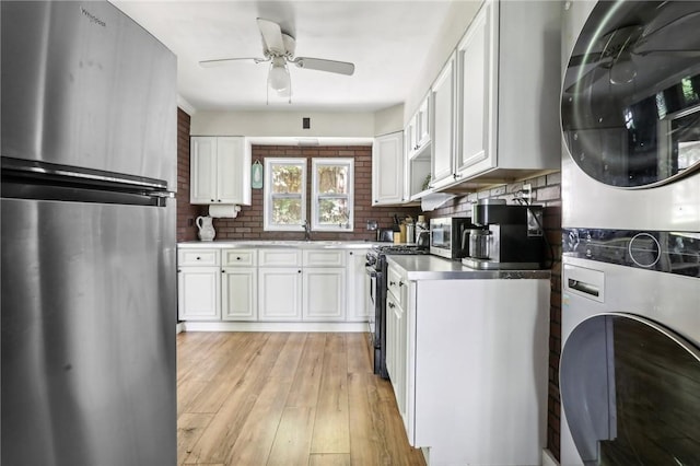 kitchen featuring stacked washer and clothes dryer, white cabinets, sink, light wood-type flooring, and appliances with stainless steel finishes