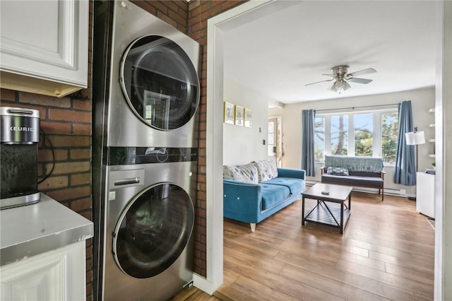 laundry room featuring ceiling fan, brick wall, stacked washer and clothes dryer, and light hardwood / wood-style floors