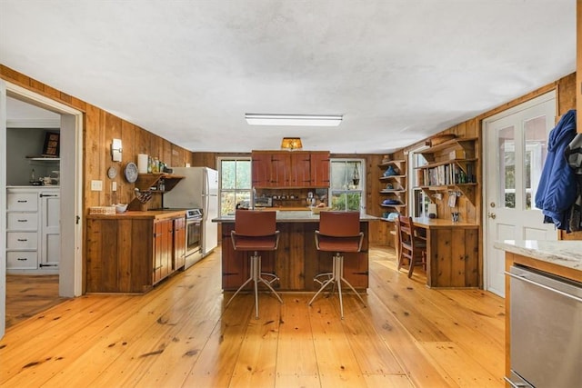 kitchen featuring wooden walls, a breakfast bar, appliances with stainless steel finishes, and light wood-type flooring