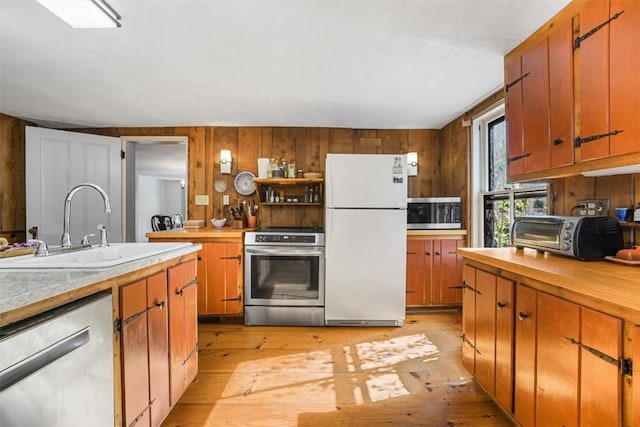 kitchen featuring wood walls, sink, light hardwood / wood-style floors, and appliances with stainless steel finishes