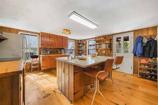 kitchen with a center island with sink, sink, light hardwood / wood-style floors, white fridge, and a kitchen bar