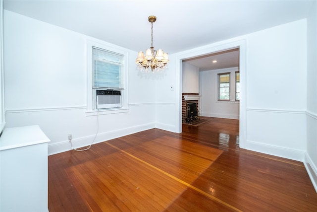 unfurnished dining area with hardwood / wood-style floors, cooling unit, a notable chandelier, and a brick fireplace