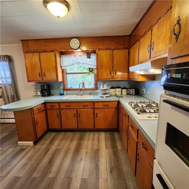 kitchen with kitchen peninsula, sink, hardwood / wood-style floors, oven, and stainless steel gas stovetop