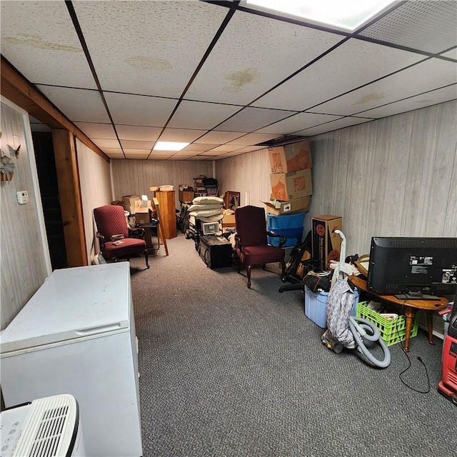 basement featuring a drop ceiling, carpet floors, and wooden walls