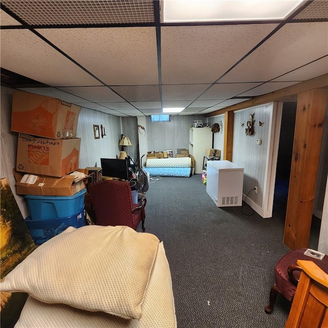 basement with carpet flooring, wood walls, and a drop ceiling