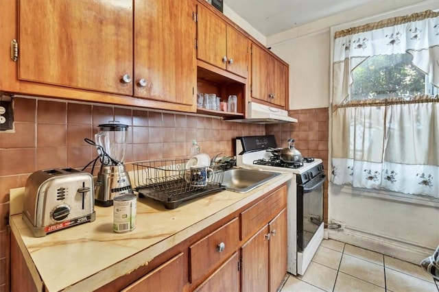 kitchen featuring sink, backsplash, white gas stove, and light tile patterned flooring