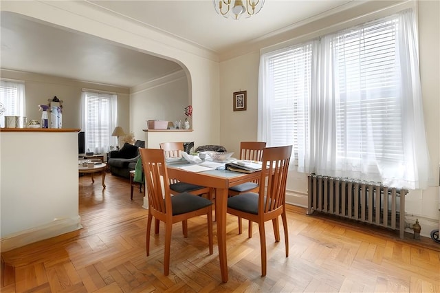 dining room featuring radiator heating unit, light parquet flooring, crown molding, and a notable chandelier