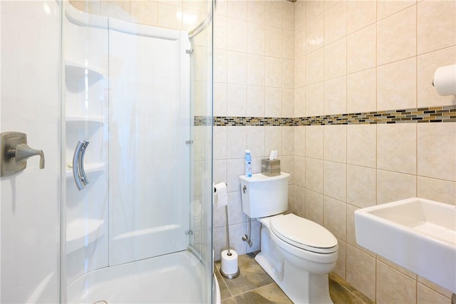 bathroom with a shower with door, sink, tile patterned flooring, toilet, and tile walls