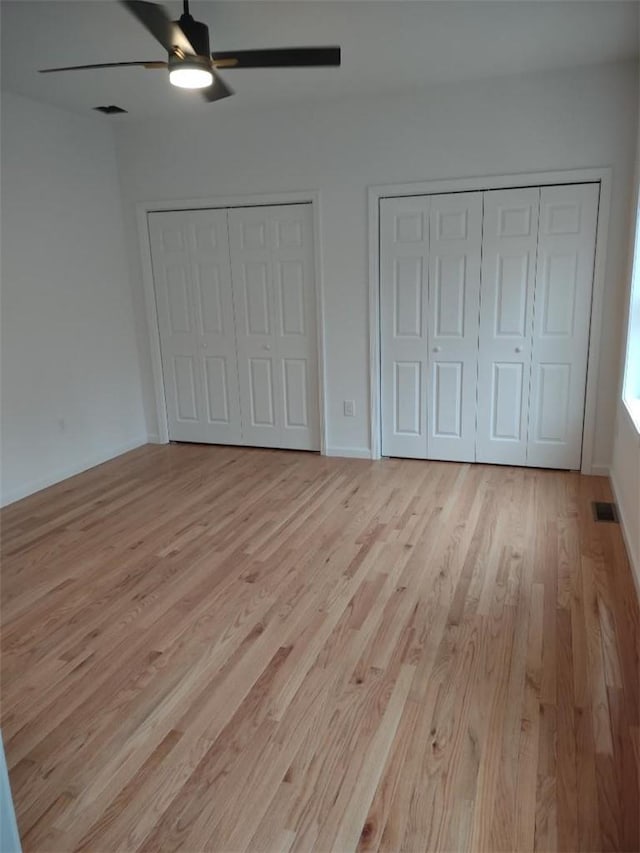 unfurnished bedroom with ceiling fan, light hardwood / wood-style flooring, and multiple closets