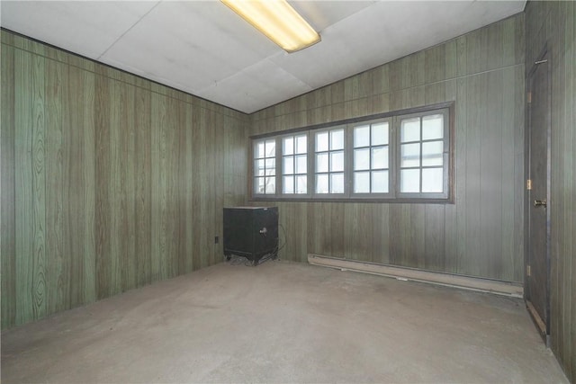 unfurnished room with lofted ceiling, baseboard heating, wooden walls, and concrete flooring