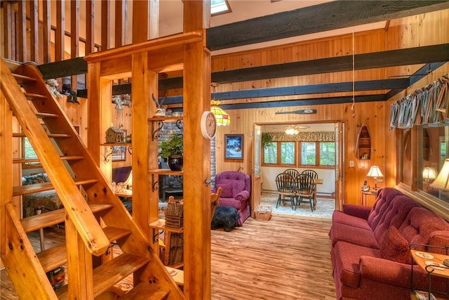 living room featuring beamed ceiling, ceiling fan, wood walls, and wood-type flooring