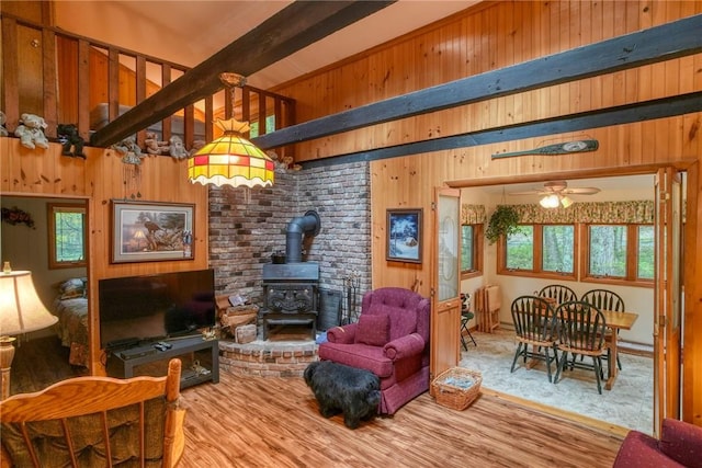 living room featuring beam ceiling, a wood stove, ceiling fan, wood walls, and wood-type flooring