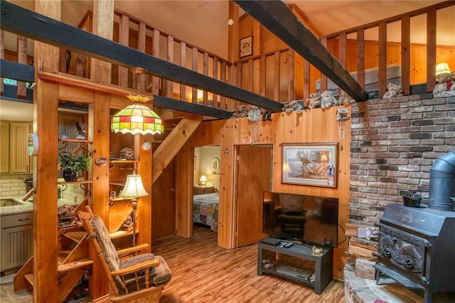 living room with a wood stove, wooden walls, a towering ceiling, and light hardwood / wood-style floors