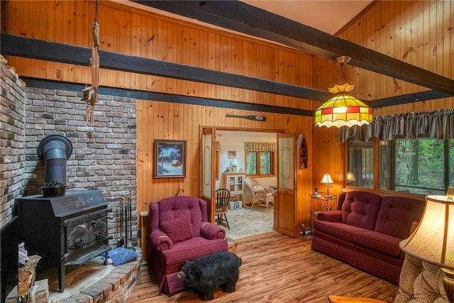 living room featuring beamed ceiling, light wood-type flooring, a wood stove, and wooden walls