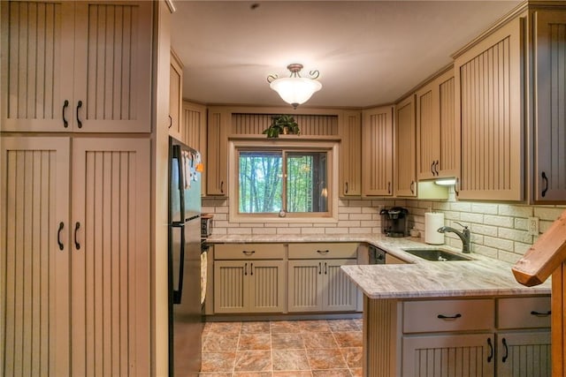 kitchen featuring kitchen peninsula, decorative backsplash, light stone counters, black fridge, and sink