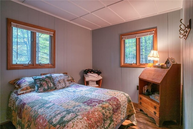 bedroom with hardwood / wood-style flooring, wooden walls, and multiple windows