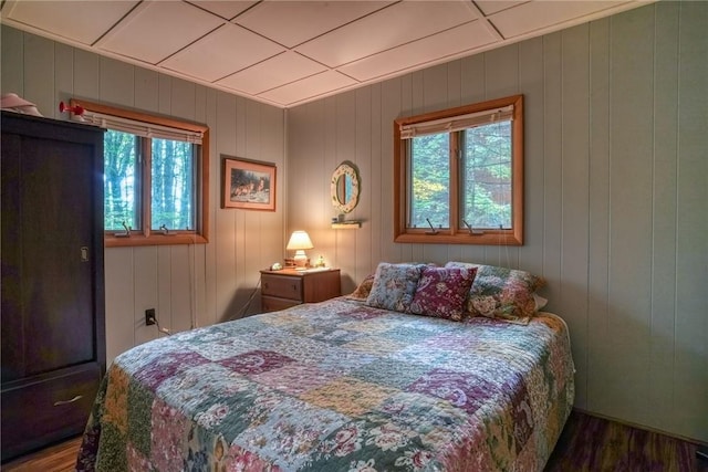 bedroom featuring multiple windows, wood walls, and dark hardwood / wood-style floors