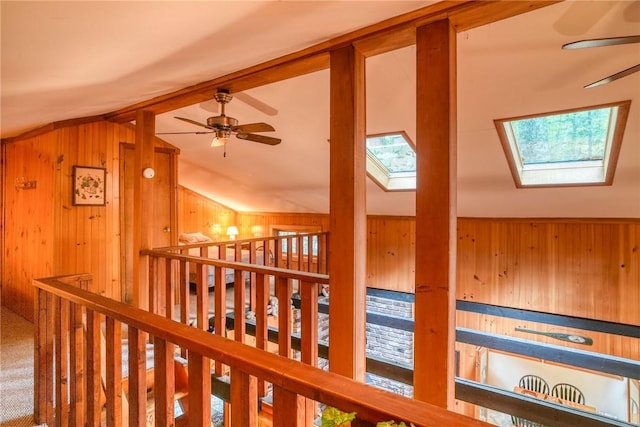 hall featuring lofted ceiling with skylight, wooden walls, and carpet