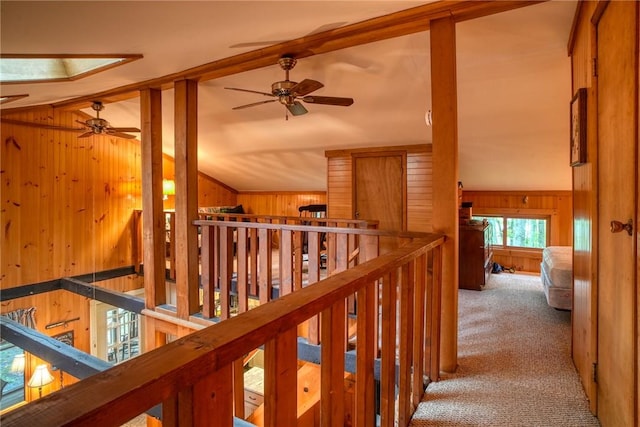 corridor with carpet flooring, lofted ceiling with skylight, and wood walls