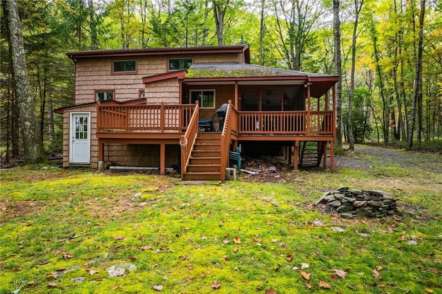 back of property with a deck, an outdoor fire pit, and a lawn