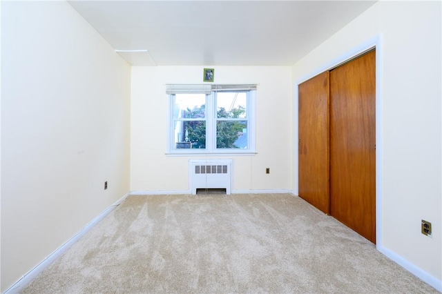 unfurnished bedroom with light carpet, radiator heating unit, and a closet