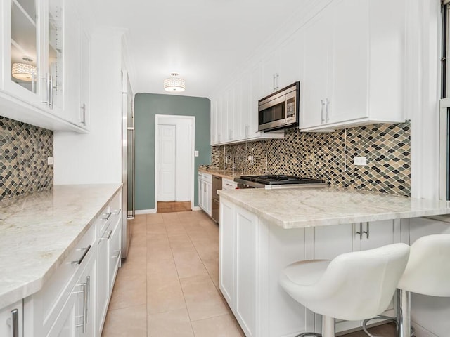 kitchen featuring white cabinets, light stone counters, a kitchen bar, and stainless steel appliances