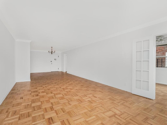 empty room with built in features, light parquet flooring, a chandelier, and ornamental molding