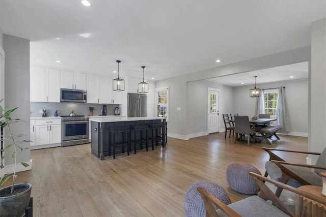 kitchen featuring white cabinetry, a center island, stainless steel appliances, light hardwood / wood-style floors, and decorative light fixtures