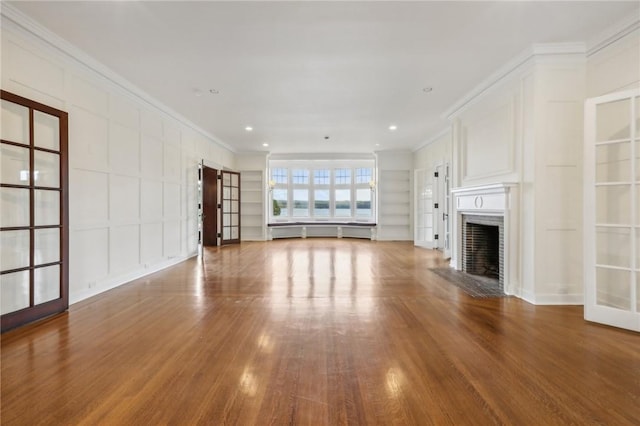 unfurnished living room with hardwood / wood-style floors, french doors, built in features, ornamental molding, and a fireplace