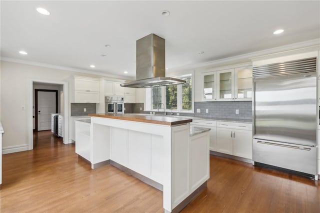 kitchen featuring appliances with stainless steel finishes, light wood-type flooring, island range hood, a kitchen island, and white cabinetry