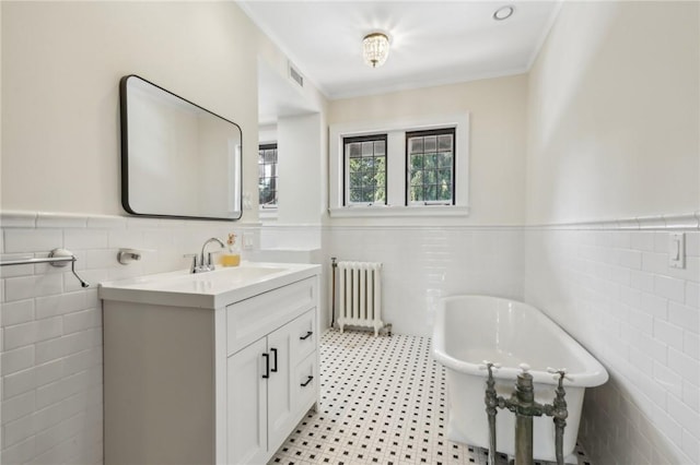 bathroom featuring radiator, a bathtub, vanity, and tile walls