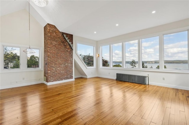 unfurnished living room featuring radiator, a water view, vaulted ceiling, and hardwood / wood-style flooring