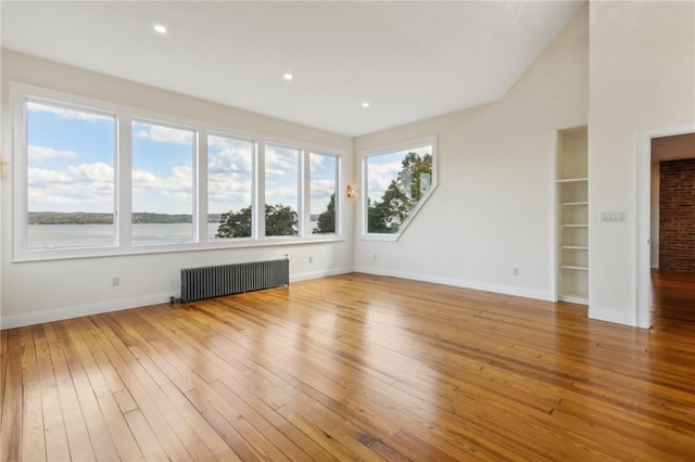 unfurnished living room featuring light wood-type flooring, a water view, and radiator