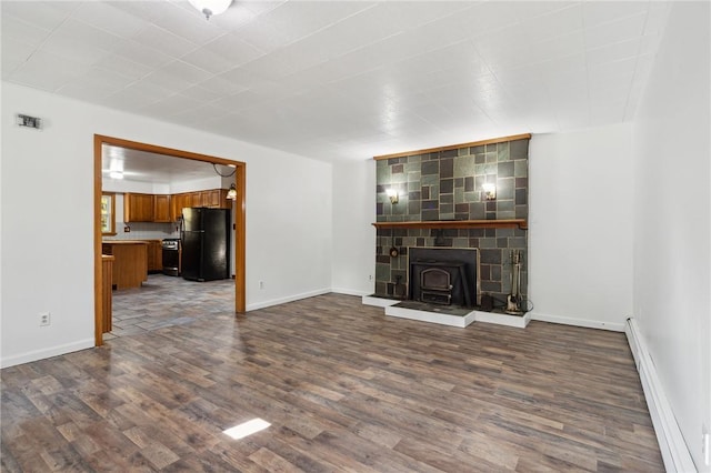 unfurnished living room with a wood stove, baseboard heating, baseboards, visible vents, and dark wood-type flooring