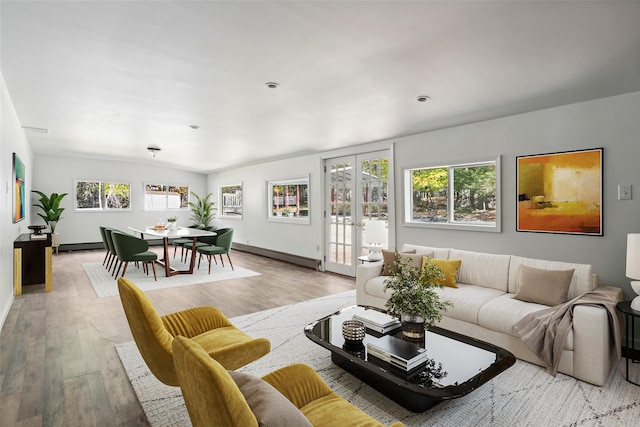 living room with plenty of natural light, light wood-style floors, a baseboard heating unit, and french doors