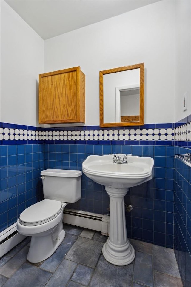 half bathroom with a baseboard radiator, a wainscoted wall, toilet, and tile walls