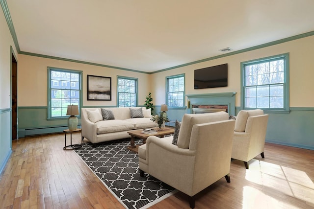 living room with light hardwood / wood-style flooring, baseboard heating, a healthy amount of sunlight, and crown molding