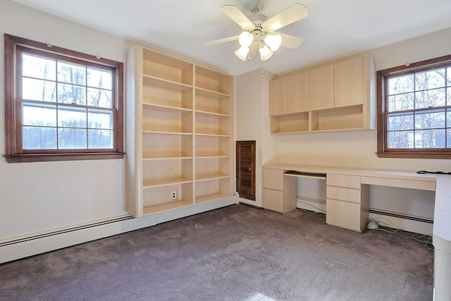 unfurnished office featuring ceiling fan, a healthy amount of sunlight, dark carpet, and a baseboard heating unit