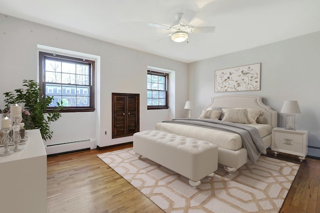 bedroom featuring a baseboard radiator, light hardwood / wood-style flooring, multiple windows, and ceiling fan