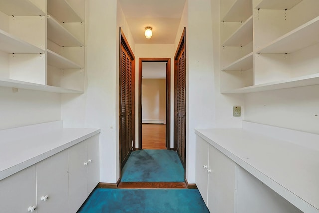 hallway with dark carpet and a baseboard heating unit