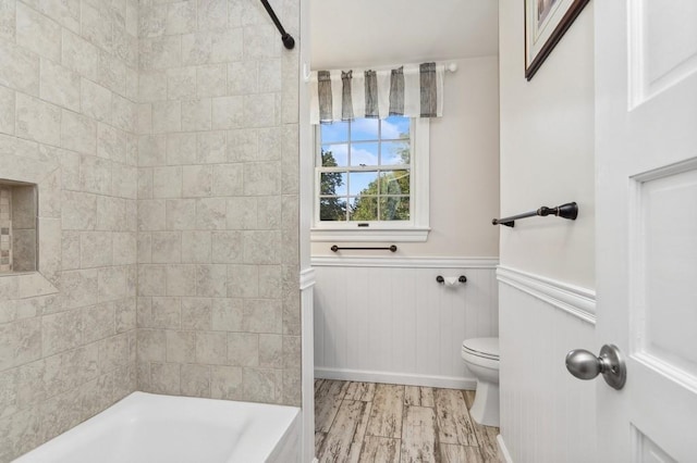 bathroom with hardwood / wood-style flooring, toilet, and tiled shower / bath